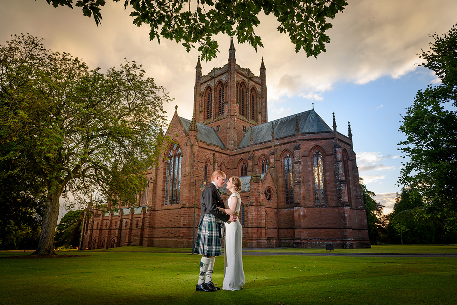 Bride and groom pose together outside The Crichton Memorial Church in Dumfries